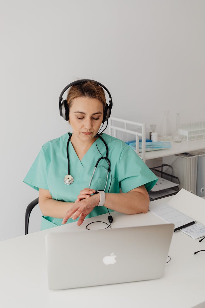 Medical professional using a laptop and smartwatch while on a call, focused on telemedicine tasks.